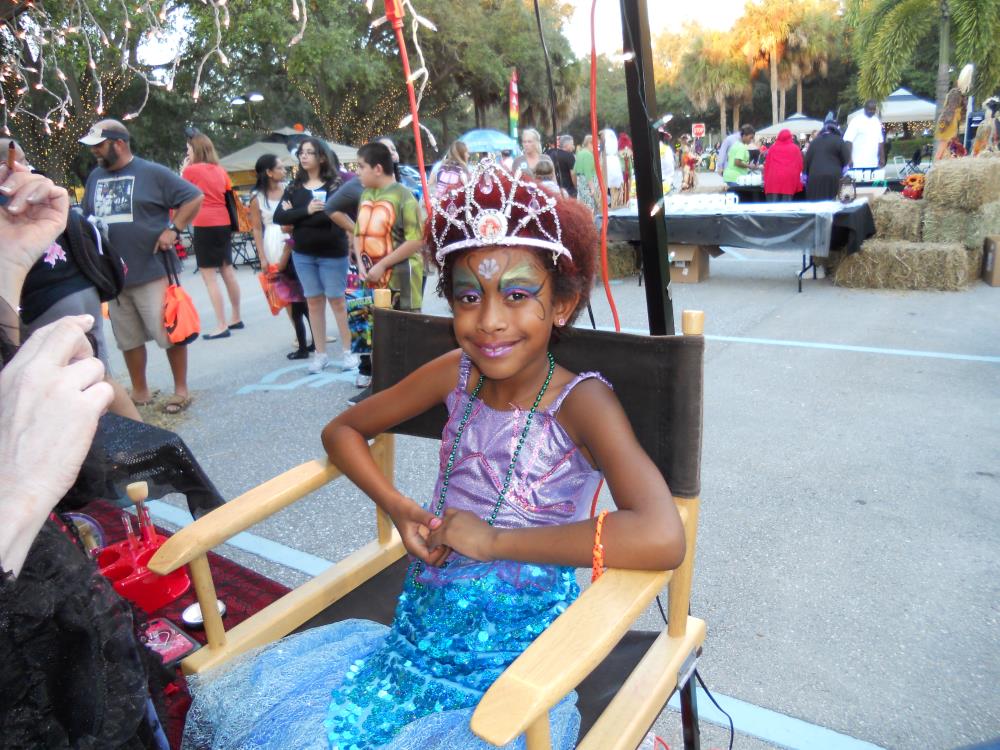 Girl dressed in purple and blue dress getting face painted